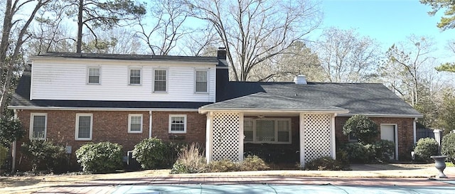 rear view of house featuring brick siding, an outdoor pool, and a chimney