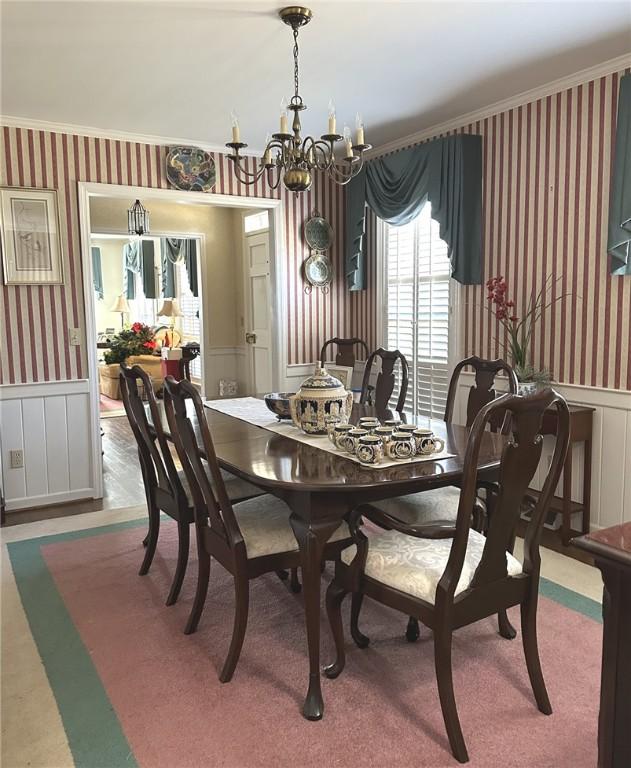 dining area with a chandelier, wainscoting, wallpapered walls, and ornamental molding