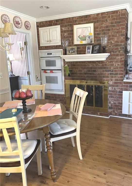 dining room featuring light wood-style flooring, a fireplace, brick wall, and ornamental molding