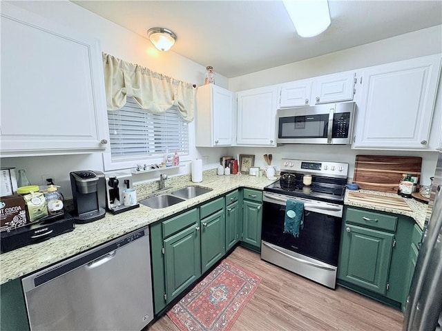 kitchen with green cabinetry, light wood-style flooring, stainless steel appliances, white cabinetry, and a sink