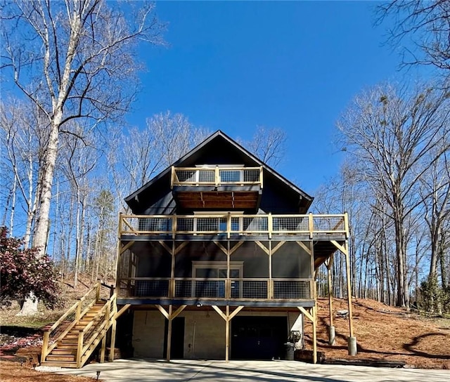 rear view of property with stairway, an attached garage, driveway, and a balcony