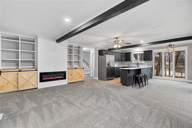 unfurnished living room featuring ceiling fan, beamed ceiling, light carpet, and a glass covered fireplace