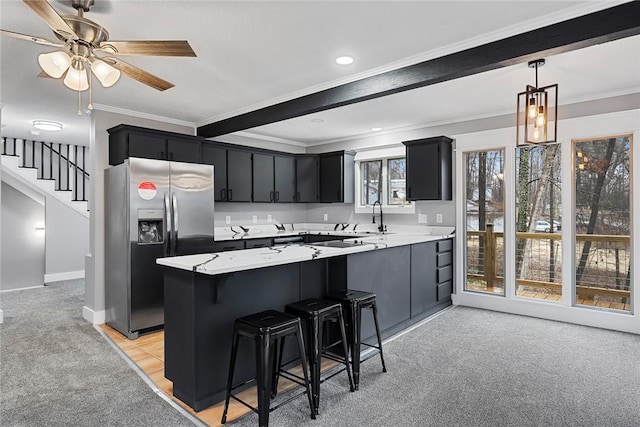 kitchen featuring a peninsula, stainless steel refrigerator with ice dispenser, pendant lighting, crown molding, and dark cabinets