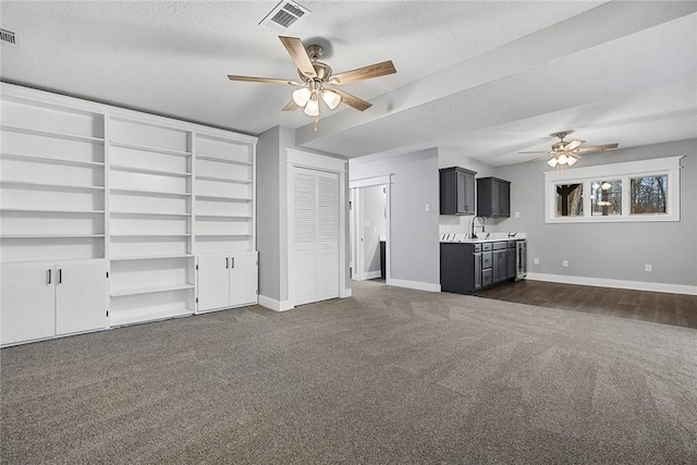 unfurnished living room featuring visible vents, baseboards, dark carpet, a textured ceiling, and a ceiling fan