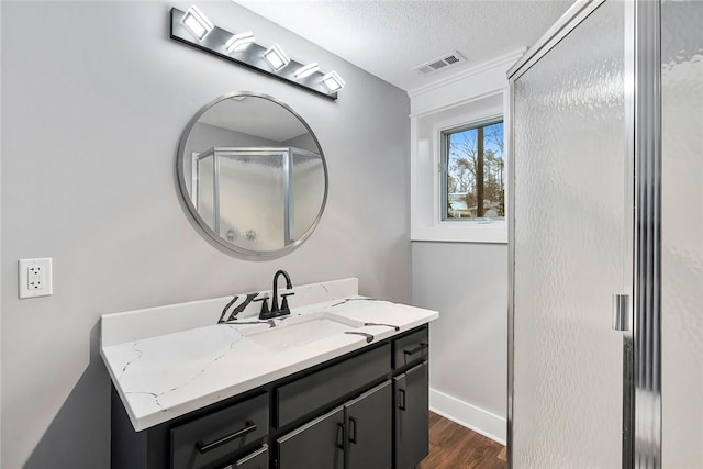 bathroom with vanity, wood finished floors, baseboards, visible vents, and a textured ceiling