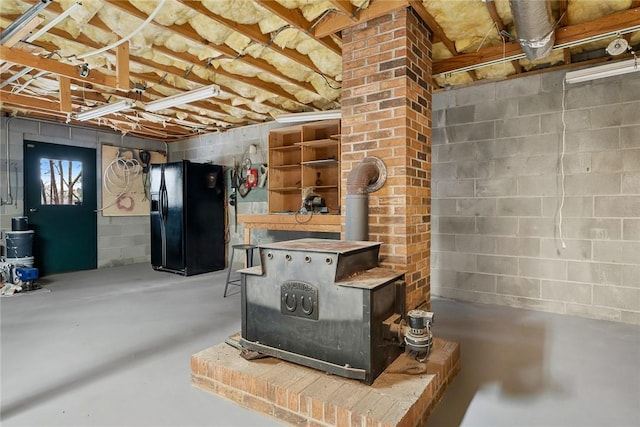 basement featuring a wood stove, concrete block wall, and black fridge