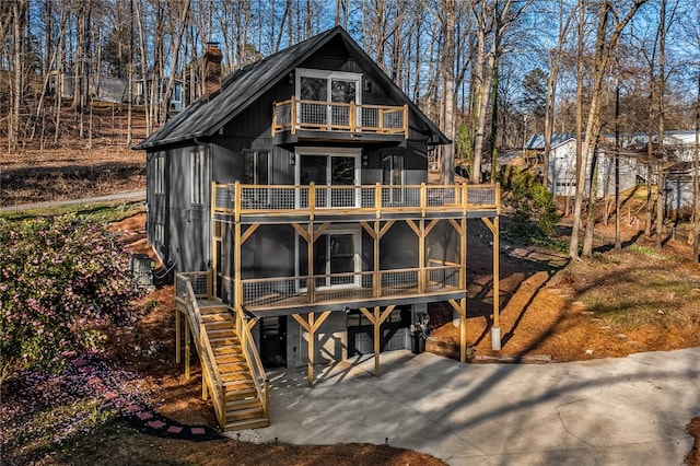 back of property with stairway, a chimney, a balcony, a sunroom, and driveway