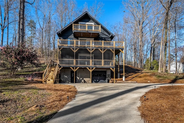 rustic home featuring concrete driveway, stairs, a balcony, a sunroom, and an attached garage