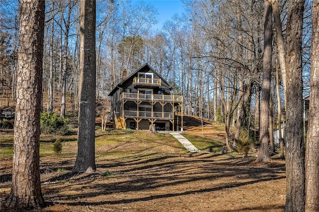 view of front of property with a front yard, a balcony, a wooden deck, and a chimney