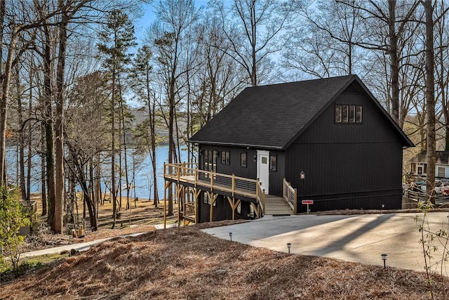 rustic home with stairs, a deck with water view, driveway, and a shingled roof