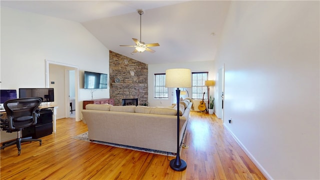 living room with baseboards, ceiling fan, a stone fireplace, light wood-style flooring, and high vaulted ceiling