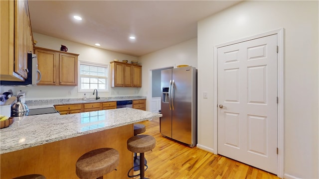 kitchen featuring a kitchen bar, a sink, light wood-style floors, appliances with stainless steel finishes, and a peninsula