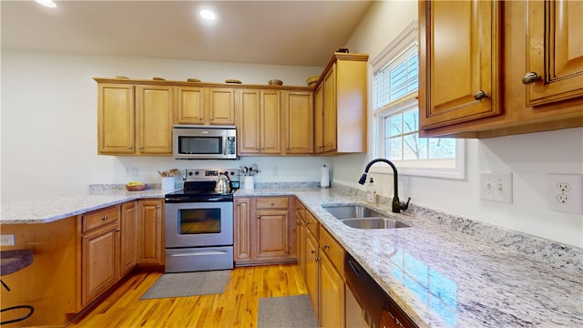 kitchen with light stone counters, appliances with stainless steel finishes, light wood-style floors, brown cabinetry, and a sink