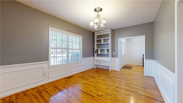 spare room featuring visible vents, a wainscoted wall, a chandelier, and light wood finished floors