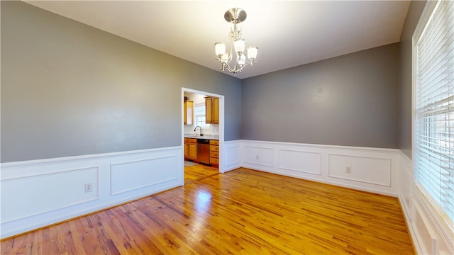 unfurnished room featuring an inviting chandelier, wainscoting, light wood-type flooring, and a sink