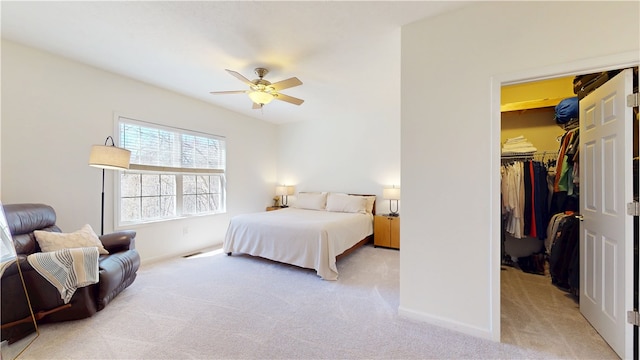 bedroom with a walk in closet, a ceiling fan, a closet, baseboards, and light colored carpet