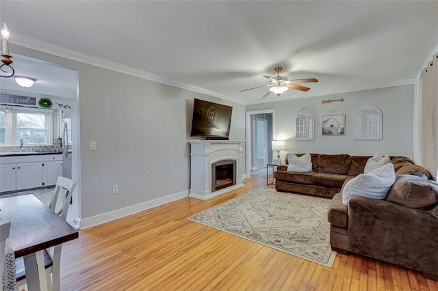 living area with light wood-style flooring, a ceiling fan, ornamental molding, a fireplace, and baseboards