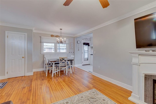 dining area with crown molding, light wood-style flooring, a fireplace, and ceiling fan with notable chandelier