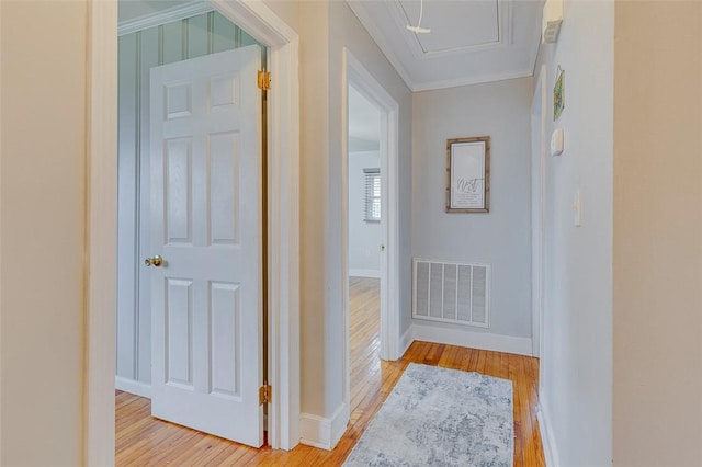 hall featuring visible vents, baseboards, crown molding, and light wood finished floors