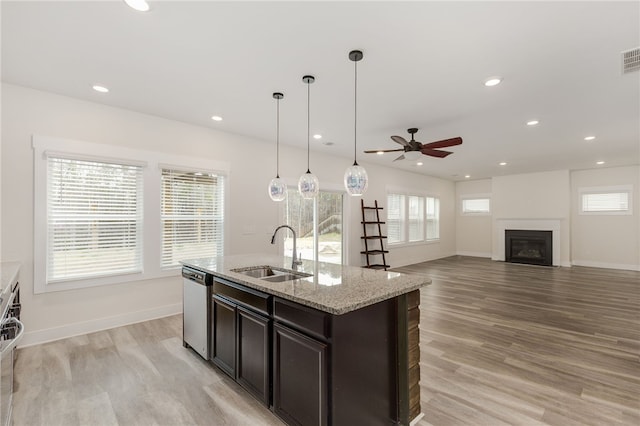 kitchen with a sink, recessed lighting, a fireplace, light wood-style floors, and stainless steel dishwasher