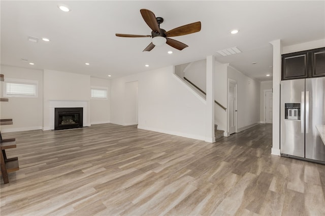 unfurnished living room with recessed lighting, stairway, light wood-style flooring, and a fireplace with flush hearth