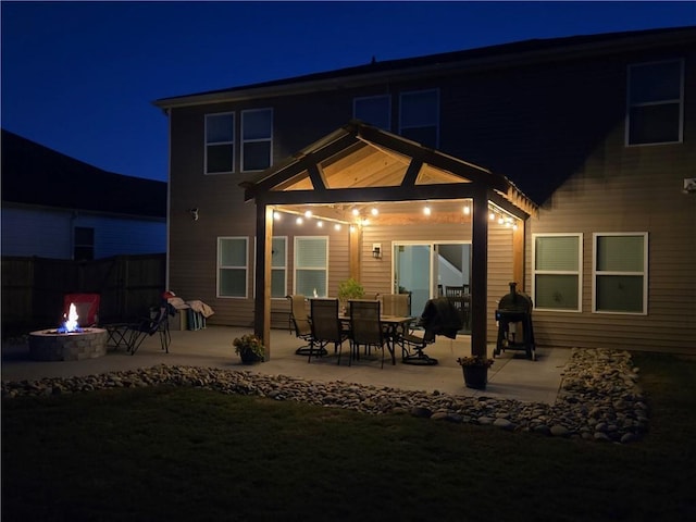 back of house at night featuring a patio, a fire pit, and fence