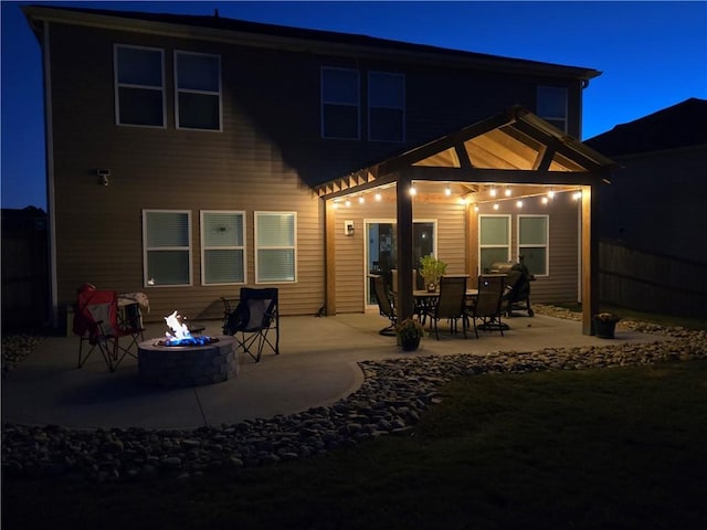 back of house at twilight with an outdoor fire pit, a patio, and fence