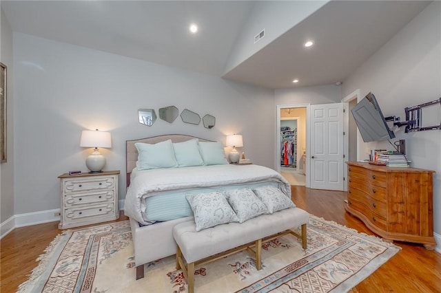 bedroom featuring visible vents, a walk in closet, wood finished floors, and vaulted ceiling