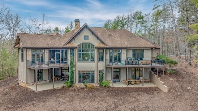 back of house with a chimney, a patio, and roof with shingles