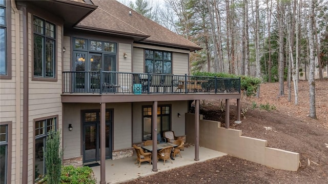 back of property with a patio area, stone siding, and roof with shingles