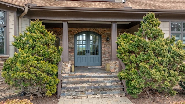 doorway to property with french doors, stone siding, and roof with shingles