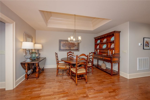 dining space featuring a raised ceiling, crown molding, visible vents, and light wood-type flooring