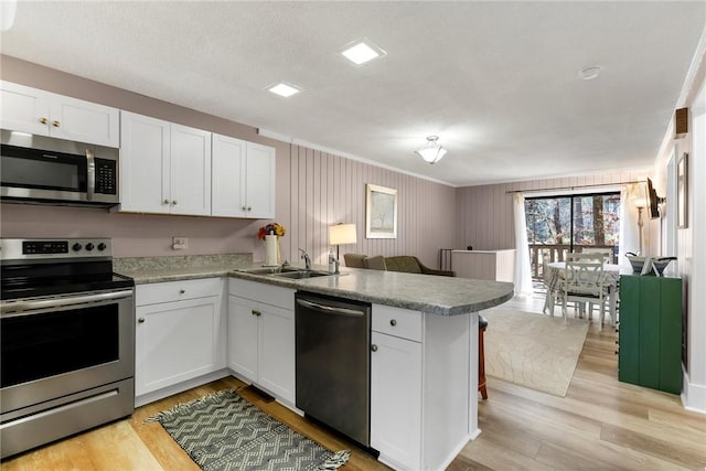 kitchen featuring a sink, a peninsula, white cabinets, and stainless steel appliances