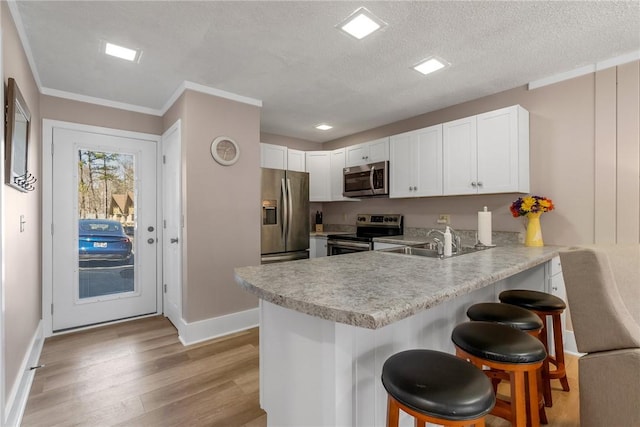 kitchen featuring a kitchen bar, light wood-style flooring, a sink, appliances with stainless steel finishes, and a peninsula