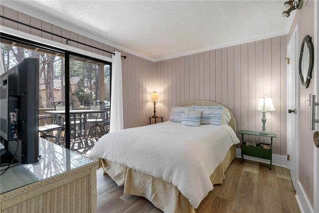 bedroom featuring access to outside, a textured ceiling, wood finished floors, crown molding, and baseboards