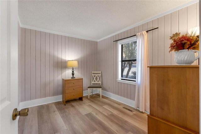 living area with a textured ceiling, crown molding, baseboards, and wood finished floors