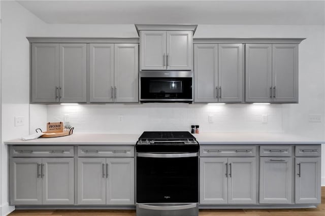 kitchen with gray cabinets, stainless steel microwave, range with gas stovetop, tasteful backsplash, and light countertops