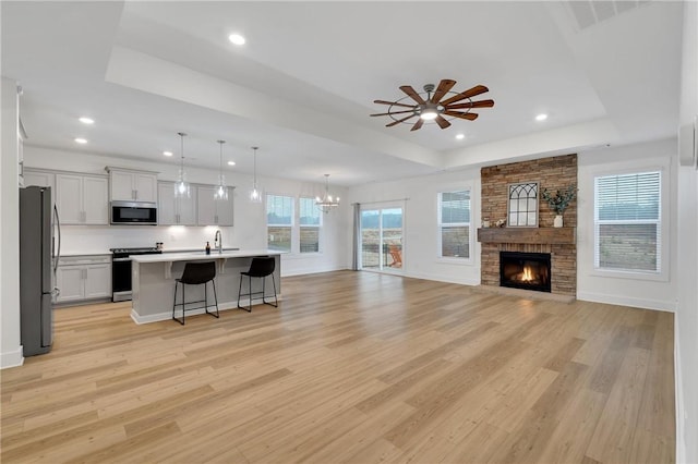 kitchen with a breakfast bar, a tray ceiling, light wood-style floors, appliances with stainless steel finishes, and open floor plan