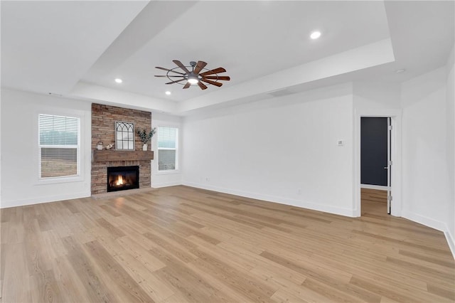 unfurnished living room with a tray ceiling, baseboards, light wood-type flooring, and a wealth of natural light