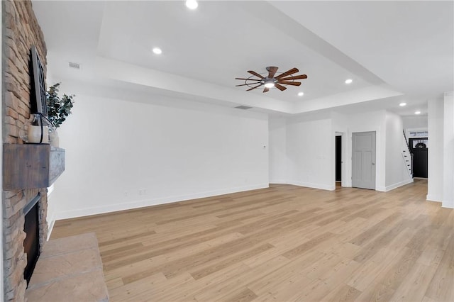 unfurnished living room featuring light wood finished floors, recessed lighting, a fireplace, and a raised ceiling