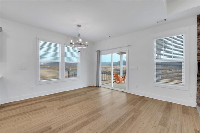 empty room featuring baseboards, a notable chandelier, and light wood-style flooring