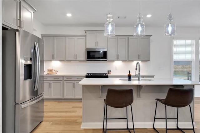 kitchen with decorative backsplash, light countertops, light wood-type flooring, and appliances with stainless steel finishes