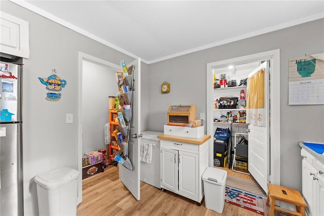 kitchen featuring light wood finished floors, crown molding, light countertops, freestanding refrigerator, and white cabinets