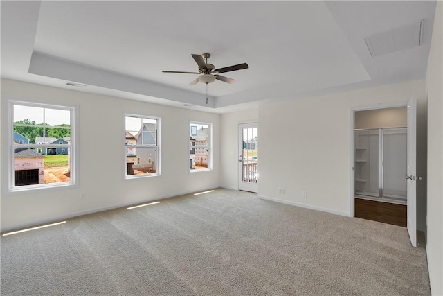 unfurnished bedroom featuring visible vents, carpet, a raised ceiling, and multiple windows