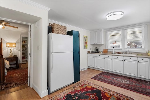 kitchen with light wood finished floors, light countertops, ornamental molding, freestanding refrigerator, and white cabinetry