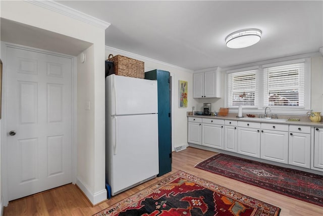 kitchen with freestanding refrigerator, a sink, light wood-style floors, white cabinetry, and crown molding