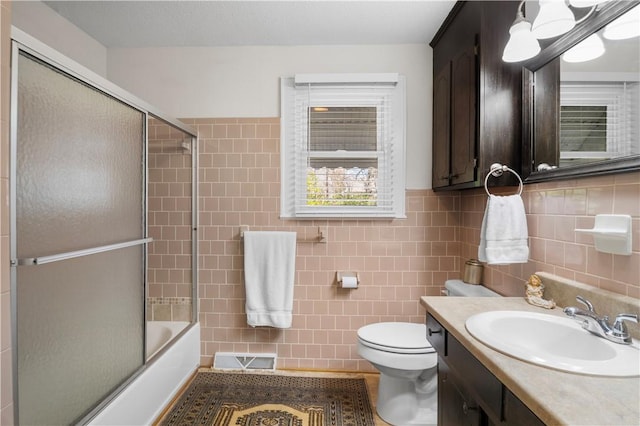 full bathroom featuring vanity, visible vents, tile walls, toilet, and combined bath / shower with glass door