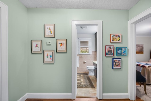 corridor with baseboards, a textured ceiling, and tile walls