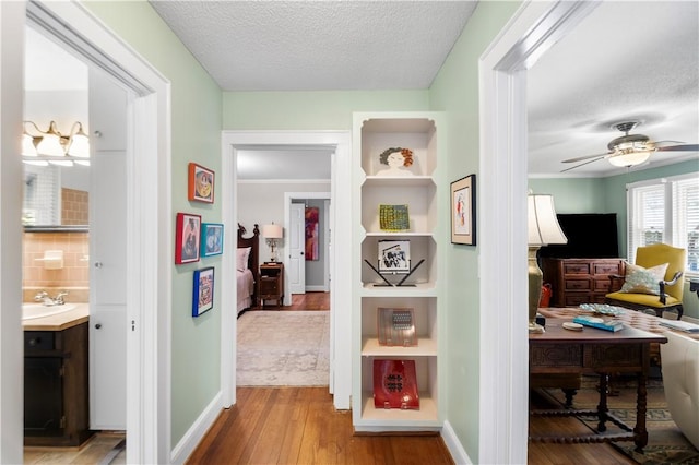 hallway with a sink, wood finished floors, baseboards, and a textured ceiling