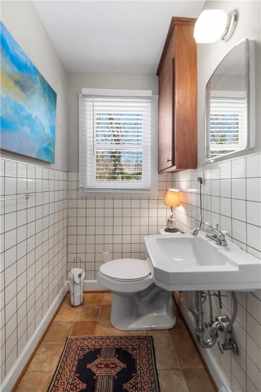 half bath with a sink, plenty of natural light, toilet, and tile walls